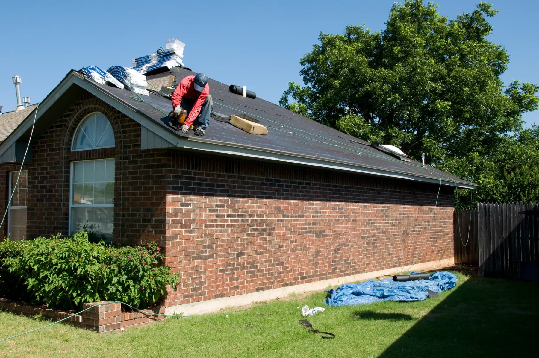 A roofer laying underlayment across the back slope of a brick ranch house