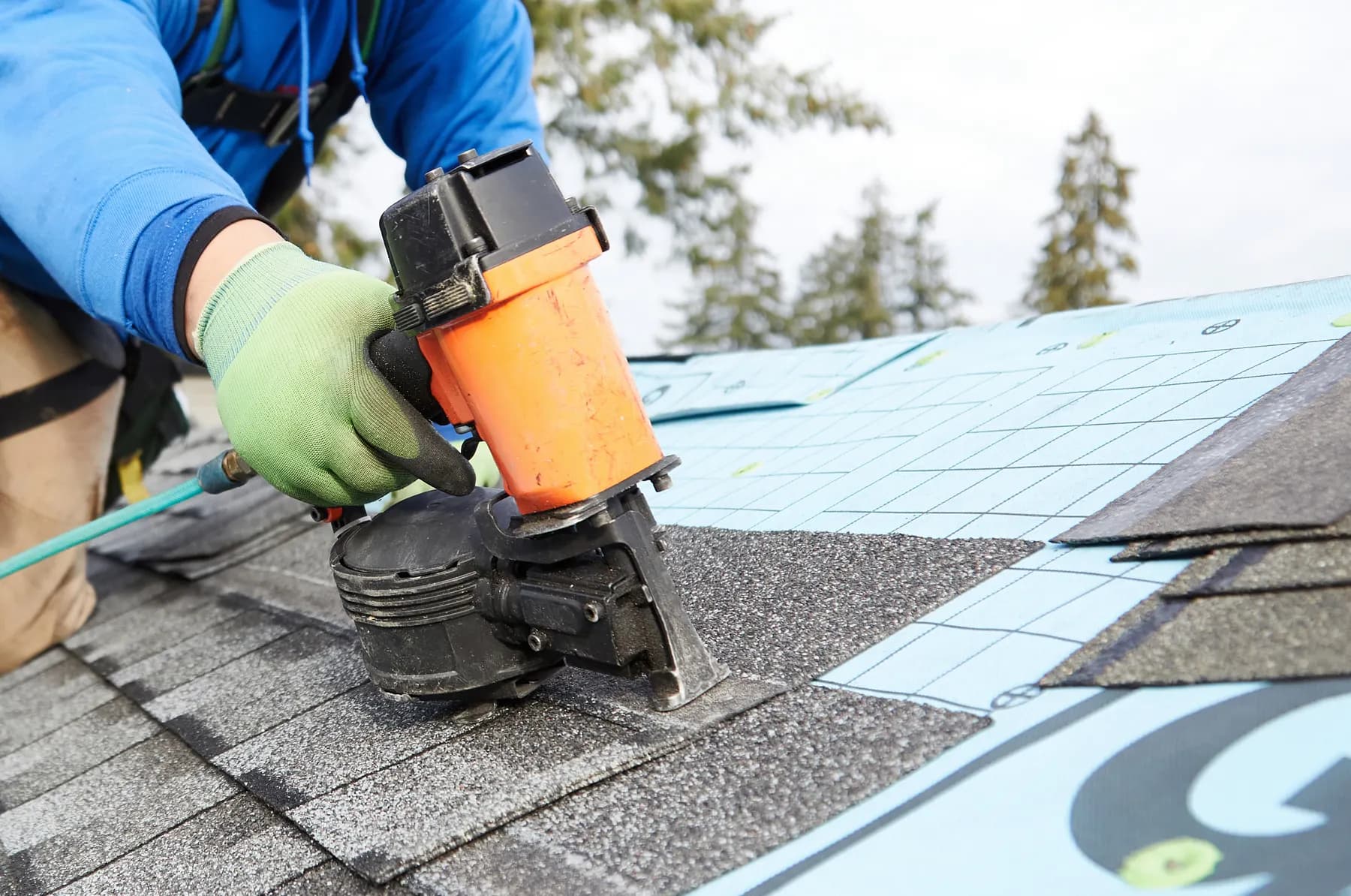 Close view of a roofer setting a fastener into a new course of shingles